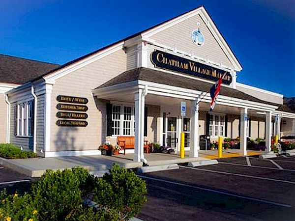 The image shows a building with a sign that reads "Chatham Village Market," featuring a porch, parking area, and an American flag.