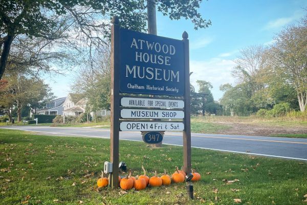 The image shows a sign for the Atwood House Museum with details, surrounded by pumpkins, and located next to a road in a green, treed area.