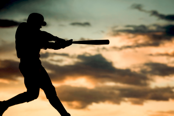 A silhouette of a baseball player swinging a bat at sunset with a dramatic sky background.