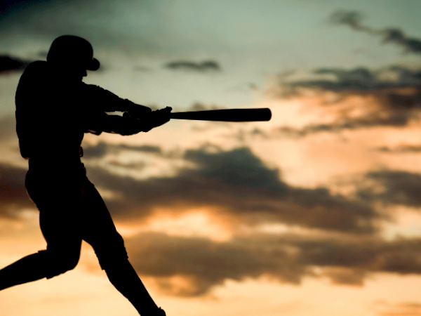 A silhouette of a baseball player swinging a bat at sunset with a dramatic sky background.
