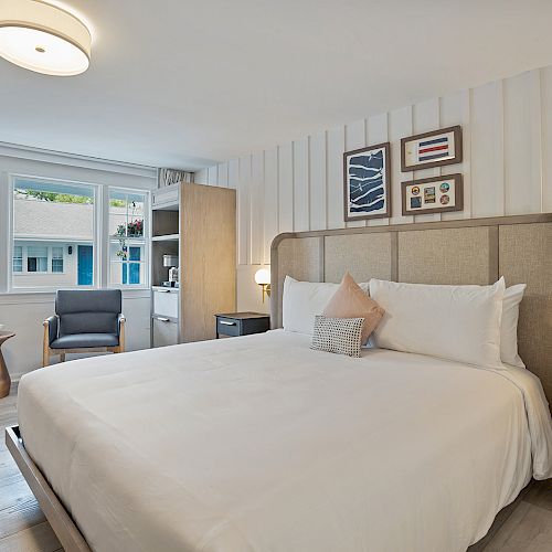 A modern bedroom with a large bed, soft lighting, wall art, and a cozy reading nook next to a large window allowing natural light.