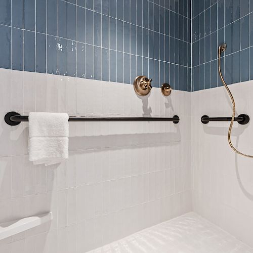 The image shows a bathroom shower area with blue and white tiles, a black grab bar with a white towel, and a handheld showerhead with a hose.