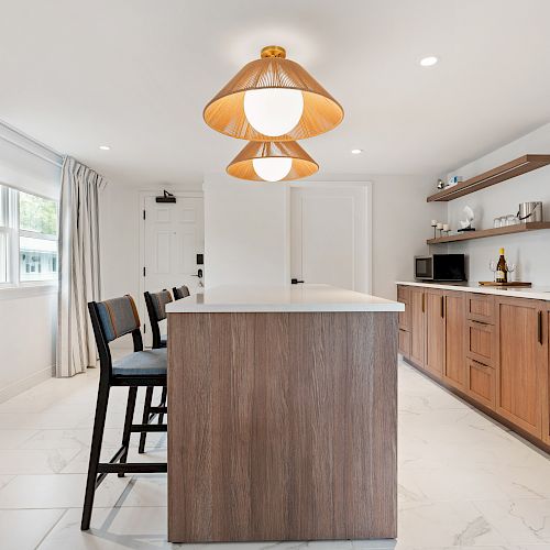 A modern kitchen with wooden cabinetry, center island with barstools, pendant lights, and open shelves, creating a clean and bright atmosphere.