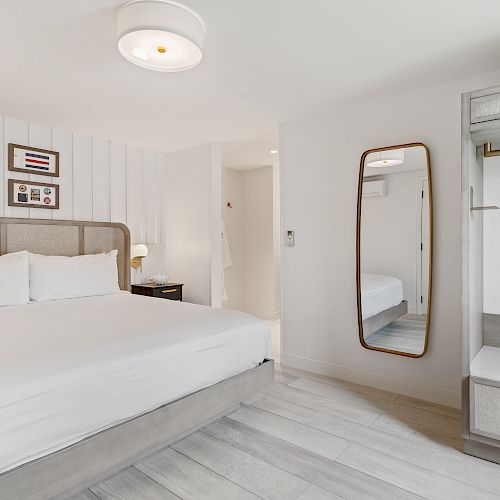 The image shows a modern bedroom with a large bed, wall art, a full-length mirror, and an open wardrobe.