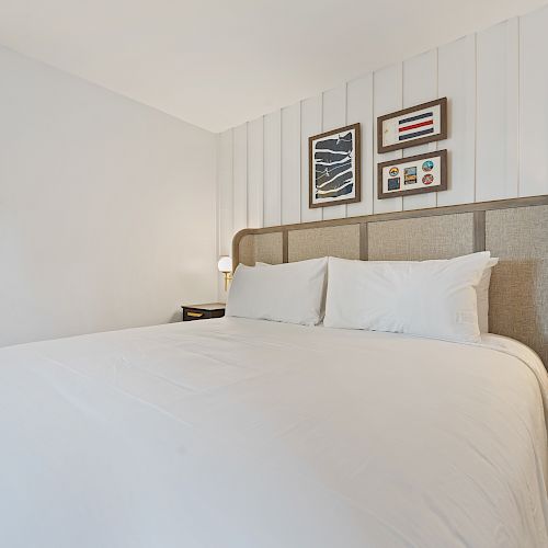 A neatly made bed with white linens, two bedside tables with lamps, and framed artwork on the wall in a minimalistic bedroom.