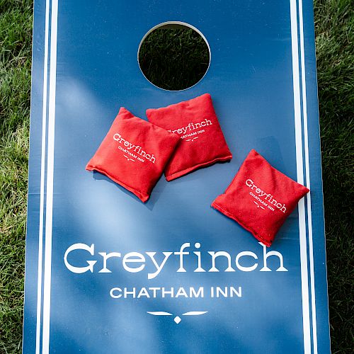 A cornhole board with "Greyfinch Chatham Inn" printed on it and three red bean bags placed on top of the board.