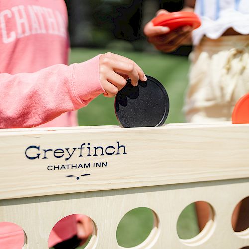 Two people play an outdoor game with red and black discs. The game set is branded 