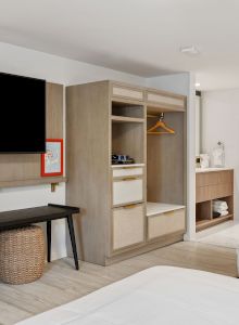 A modern hotel room features a large TV, open wardrobe, small desk with a chair, and a bathroom area with robes hanging on hooks, ending the sentence.