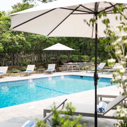 The image shows a serene outdoor pool area with umbrellas, lounge chairs, and lush greenery, perfect for relaxation and leisure.