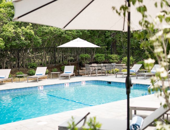 The image shows a serene outdoor pool area with umbrellas, lounge chairs, and lush greenery, perfect for relaxation and leisure.