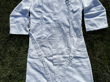 The image shows a white martial arts gi (uniform) with long sleeves, lying on grass.