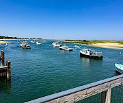 Boats moored in a marina by a sandy beach, with calm blue water and a bright, cloud-dotted sky.