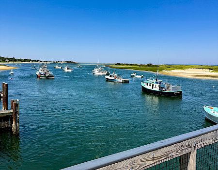 Boats moored in a marina by a sandy beach, with calm blue water and a bright, cloud-dotted sky.