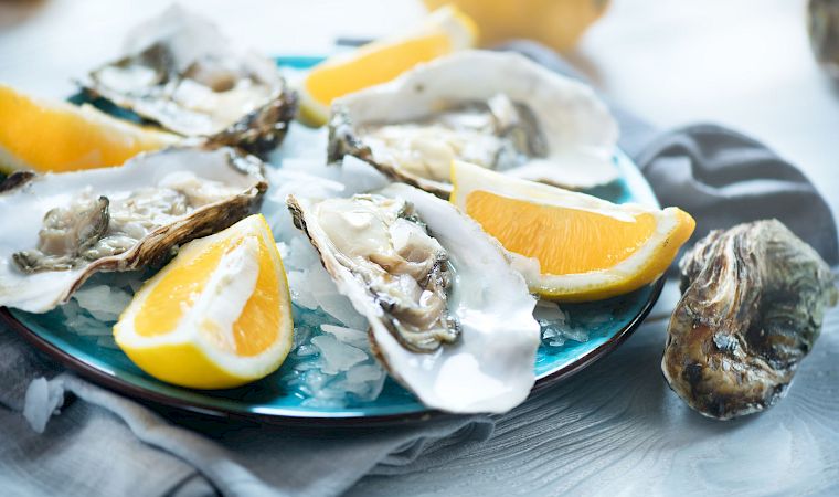 Fresh oysters on a bed of ice, topped with lemon wedges, for a chilled seafood platter.