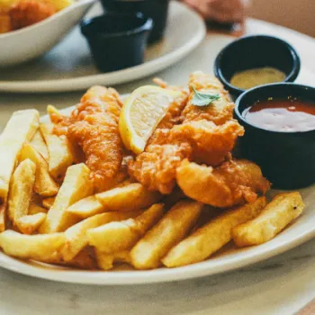 A plate of golden French fries and fried chicken pieces with lemon and three dipping sauces.
