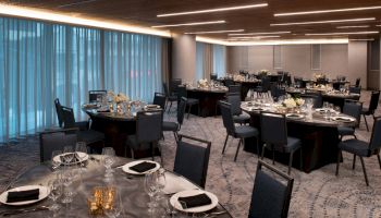 A modern banquet hall with round tables set for a formal event, featuring elegant black chairs and decor, softened by dim lighting and curtains.