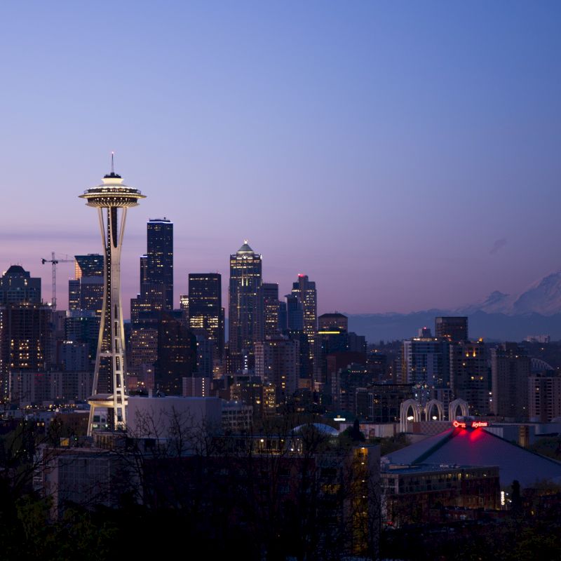The image shows a nighttime skyline of Seattle with the Space Needle prominently visible, and Mount Rainier in the background.