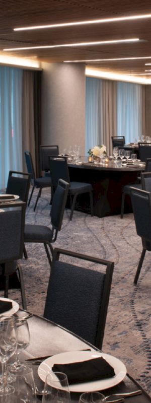 The image shows an elegantly set dining room with round tables, black chairs, and dim lighting, suitable for a banquet or formal event.