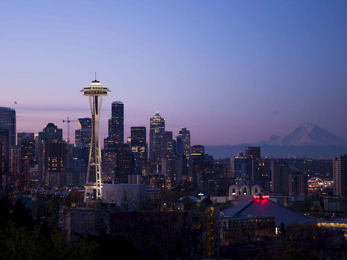 The image depicts the Seattle skyline at dusk, featuring the iconic Space Needle with Mount Rainier visible in the background.