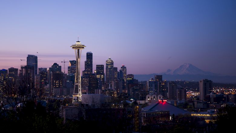 The image depicts the Seattle skyline at dusk, featuring the iconic Space Needle with Mount Rainier visible in the background.